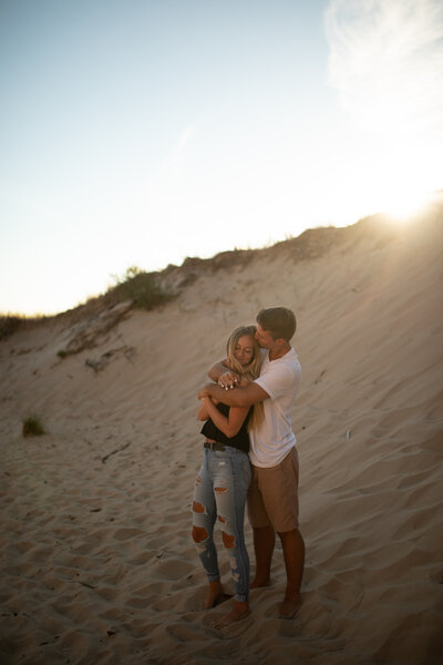 Boy hugging a girl from behind and kissing her on the cheek at sunset