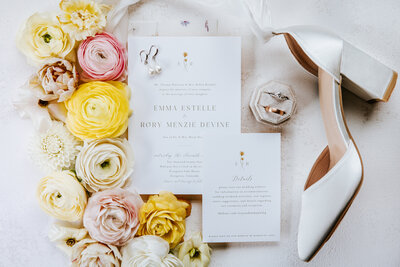 Beautiful flat lay of inviations, shoes, wedding rings, and flowers.