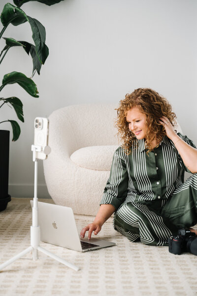 Woman with red curly hair leans on the arm of a chartreuse  couch