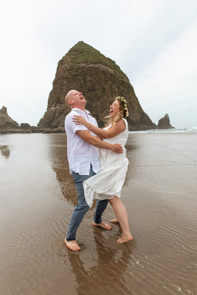 Couple embraces and laughs on the beach, in front of Haystack Rock, immediately following their wedding in Canon Beach, Oregon.
