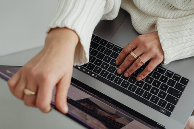 kaboompics_woman-in-white-sweater-gold-rings-jewelry-jeans-laptop-work-29445