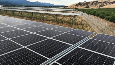 Large ground-mounted solar panel installation on a rural site with mountain and farmland views in the background
