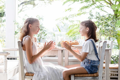 Two young girls sit at a sunlit dining table playing a hand-clapping game together – Family Autism Support Coach at Chantal Hewitt Coaching