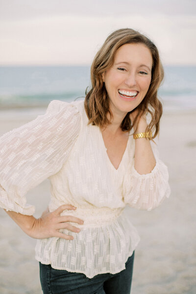 Wedding photographer, Catherine Taylor, smiles on the beach in a white blouse
