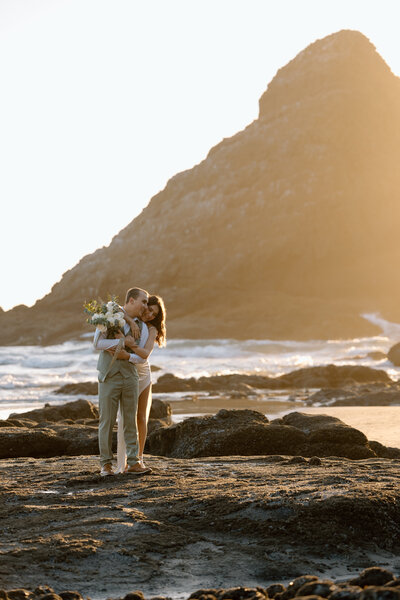 Elopement couple embracing while standing on an Oregon Coast beach.