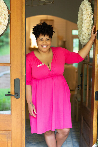 A realtor in pink dress smiles and poses in front of an open door in a Hoover Alabama model home.