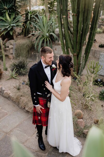 A wide overheard view of a wedding couple as they wrap their arms around each other in David Welch Winter Gardens in Aberdeen. They are surrounded by cacti in a botanical glasshouse.