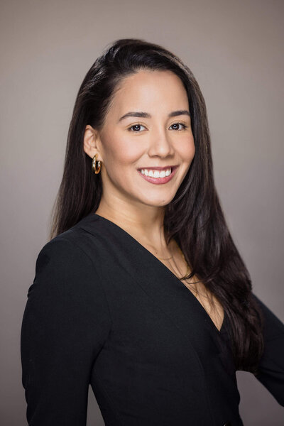 Professional headshot of a business woman in a black blazer smiling on a neutral background, Long Island corporate headshots.