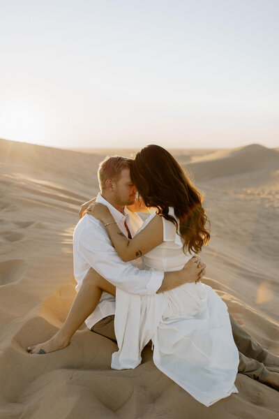 couple sitting on top of each other in sand dunes