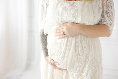 Mom holding baby bump wearing a cream lace dress in a studio in Savannah, Ga with Constance Calton photography