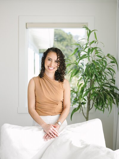 Woman standing in front of a white couch and green plant during her brand session in NYC with Krista Marie