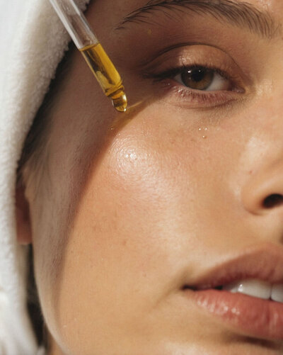 close up view of womans face while she is applying a dropper of serum to her skin