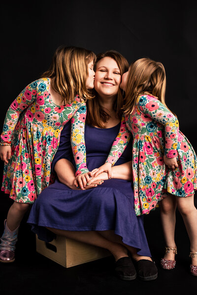 A mother and her two daughters embrace in the Pittsburgh photography studio on a solid black backdrop.