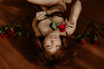 african american woman laying on the ground in black lingerie holding a rose