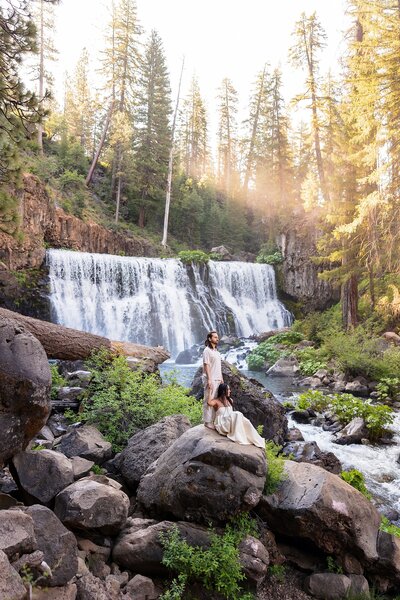 cute couple sitting on waterfall rocks