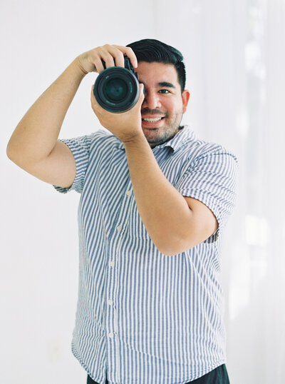 Photographer Headshot with his camera to his eyes for that fun effortless photo in an all white indoor studio