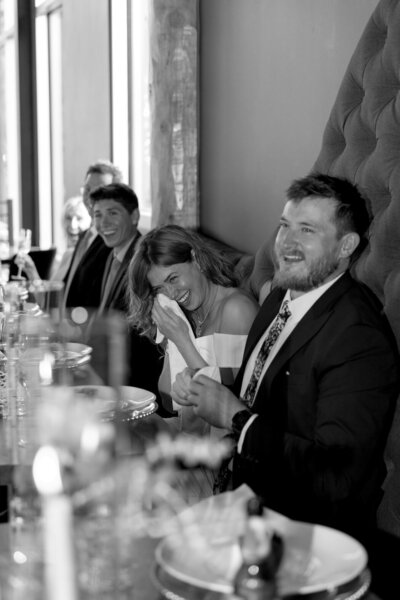Rehearsal dinner guests laughing together at a long candlelit table — documentary wedding weekend coverage in Colorado
