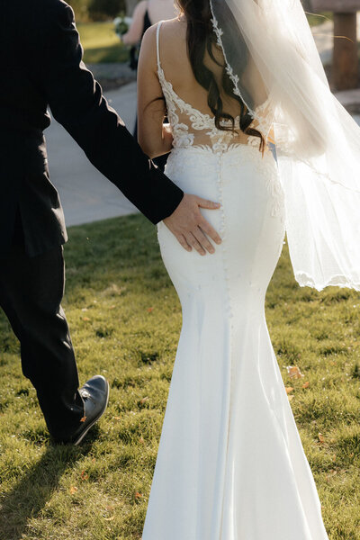 Groom’s hand on the bride’s back as they walk in sunlight
