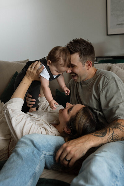 Warm black-and-white family photo of parents and their baby enjoying a cozy moment on the couch, showcasing the joys of parenthood.