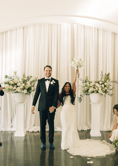 A bride raises her white bouquet while standing at the altar about to end her ceremony with her groom
