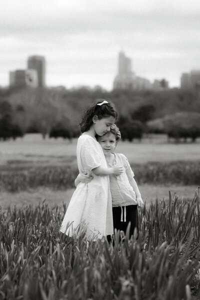 young siblings hugging in a field with raleigh skyline