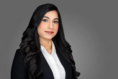 Corporate professional headshot of woman in dark blazer and white blouse against gray studio background