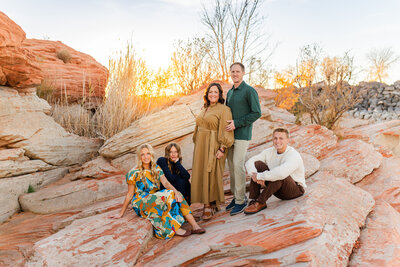 mom, dad, and two boys snuggling and playing together while sitting on the red rocks at snow canyon state park in st george utah