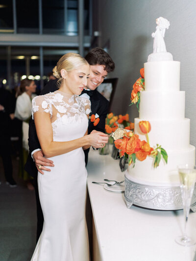 Bride and groom cutting their white tiered cake decorated with orange flowers