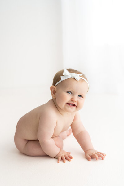 Baby girl sitting up and smiling brightly at camera