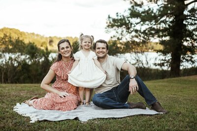 family picture with toddler on blanket in grass in front of a pon