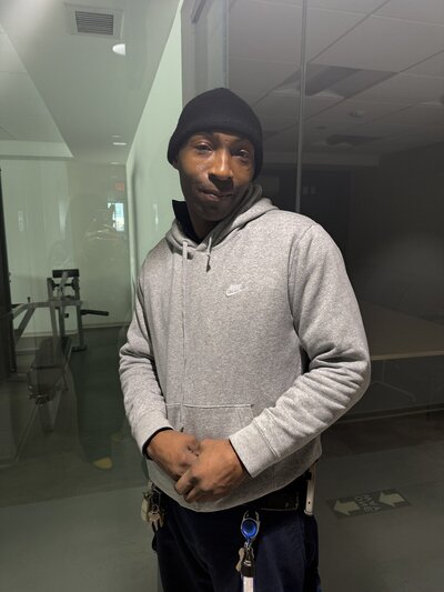 man in a black beanie and grey hoodie standing with his hands in front of his waist