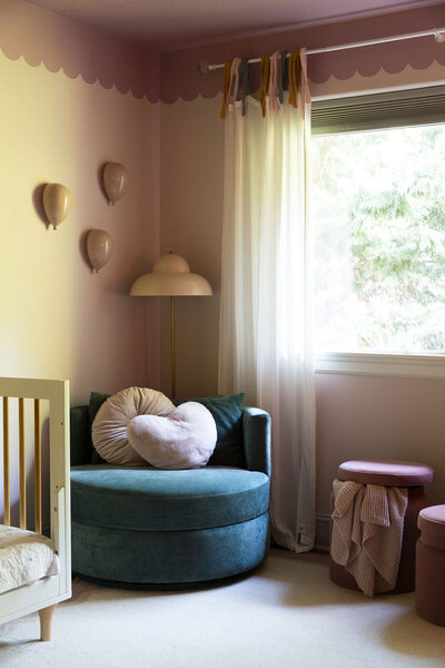 A corner of a bedroom featuring a chair, lamp, wall decoration and window curtains representing colorful home decor.