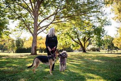 Audrie Meyer walking with her dogs in a park, symbolizing balance, calm, and clarity achieved through spiritual coaching and healing.