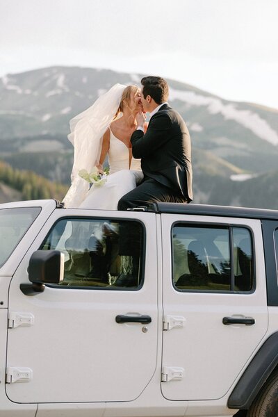 Bride and groom kiss on top of Jeep during Rocky Mountain off-road elopement.