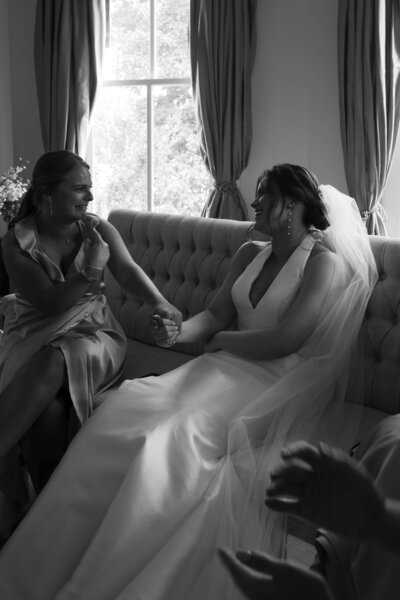 A bride is having a moment with her bridesmaids and they are holding hands laughing together