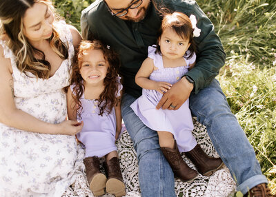 Young Sisters wearing purple dresses and cowboy boots sitting on a blanket during a spring family photo session in La Verne, California