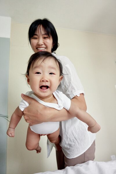 A mother with a large chest tattoo is half-hugging and smiling at her young daughter, who is wearing a red skirt with black spots.