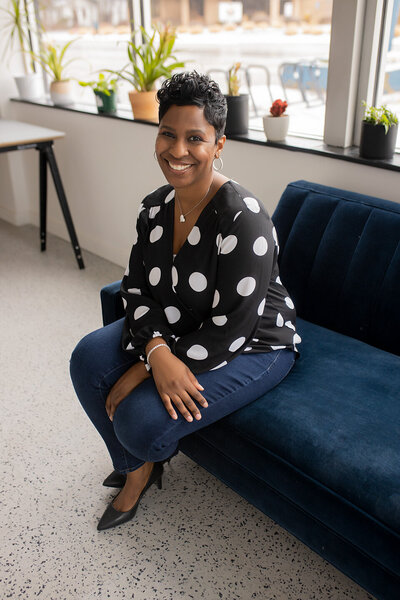 Metro Detroit Portrait Photographer with short pixie haircut in black polka dot blouse and blue jean jeggings posing casually