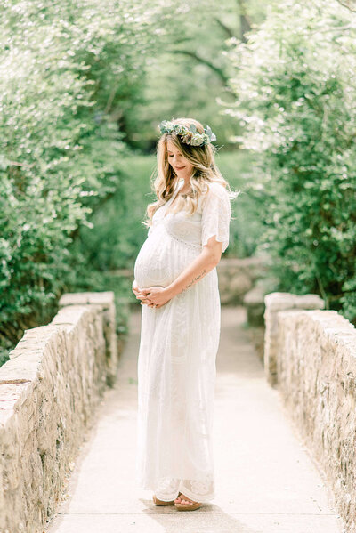 Woman in white maternity dress holds her bump on Highland Park bridge in Dallas