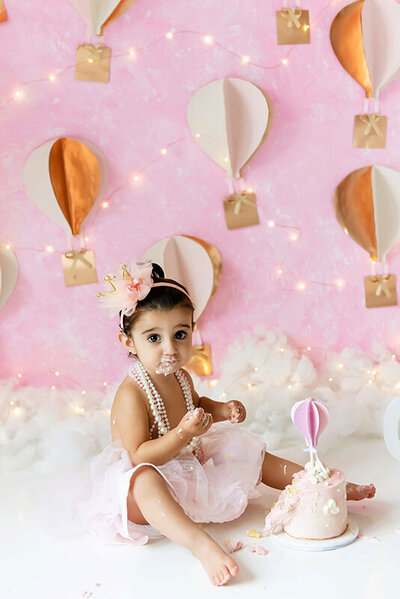 little girl wearing pink sitting in front of her hot air balloon cake smash session in Burlington, Ontario.