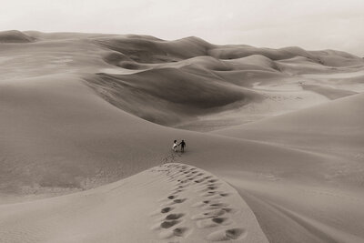 bride and groom walking through sand dunes