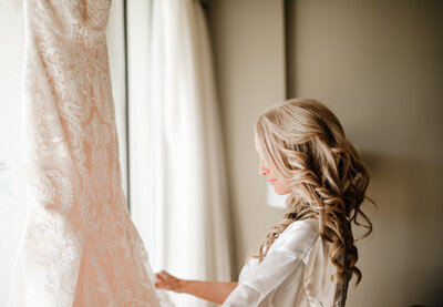 bride admiring her dress hanging in the window at hotel before wedding