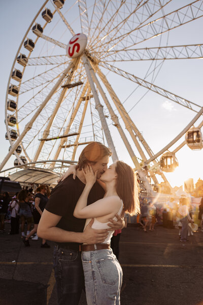 couple kissing in front of a ferris wheel at the calgary stampede