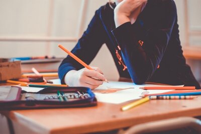 A student holds a colored pencil over a drawing they're engaged with.