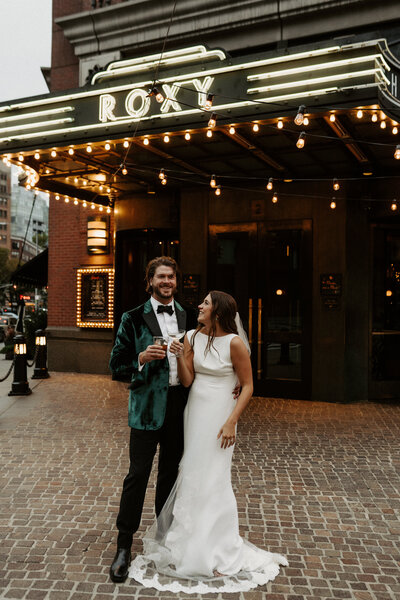 couple standing in front of roxy hotel with drinks in hand
