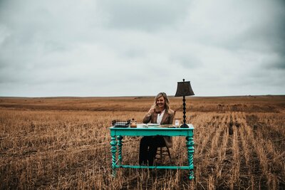 women consultant sits at a desk in a field during a brand photography session in southern Saskatchewan 