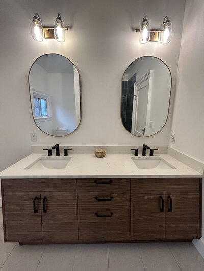 Brown vanite with white countertop. two vertical oval mirrors, and black fixtures