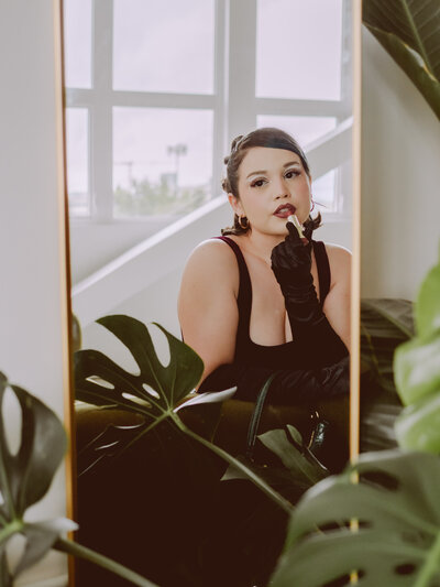 Confident woman in black gloves applying lipstick in front of a mirror framed by monstera leaves – bold branding photo by Mewphotovideo in The Studio Lab