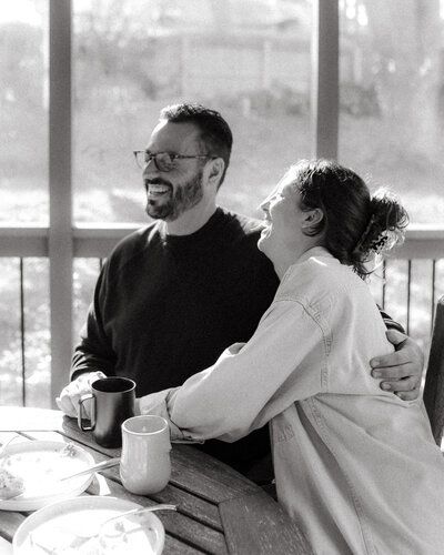 a couple laughing over breakfast during their in home engagement session Columbia, MO