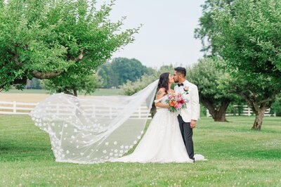 A bride and groom kiss as her veil flies in the wind. 